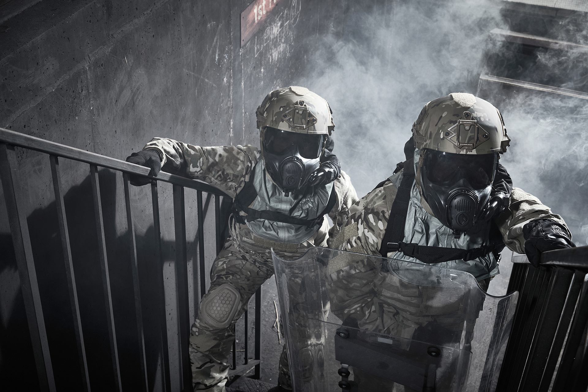 Two soldiers on staircase wearing ballistic helmets and respirators