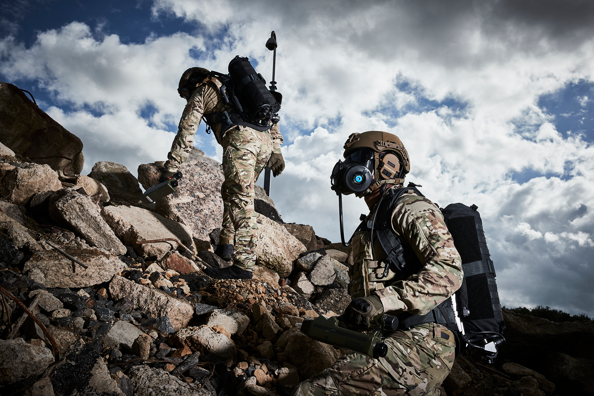 Two soldiers climbing a rubble pile wearing helmets and respirators